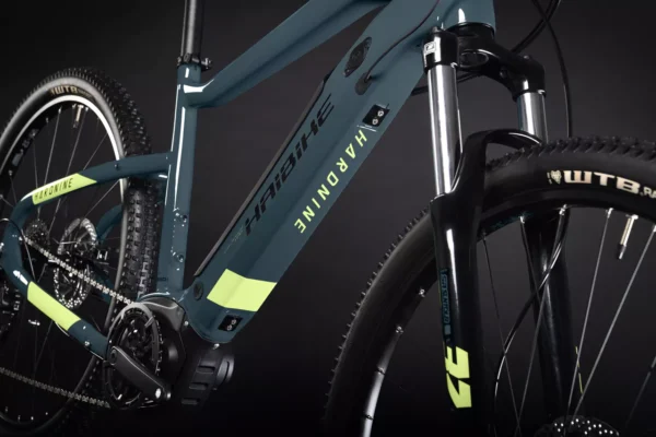 Una bicicleta eléctrica de montaña Haibike HardNine 5.0, diseñada para aventuras en terrenos desafiantes. Su cuadro de aluminio azul con detalles amarillos integra componentes Bosch de alto rendimiento y ruedas de 29", ideal para explorar senderos.