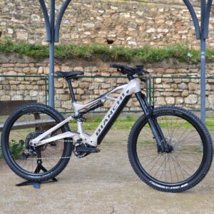 Bicicleta eléctrica de montaña Bianchi E-Vertic FX-Type con doble suspensión, motor central integrado y neumáticos Schwalbe Nobby Nic, estacionada en un entorno rural.