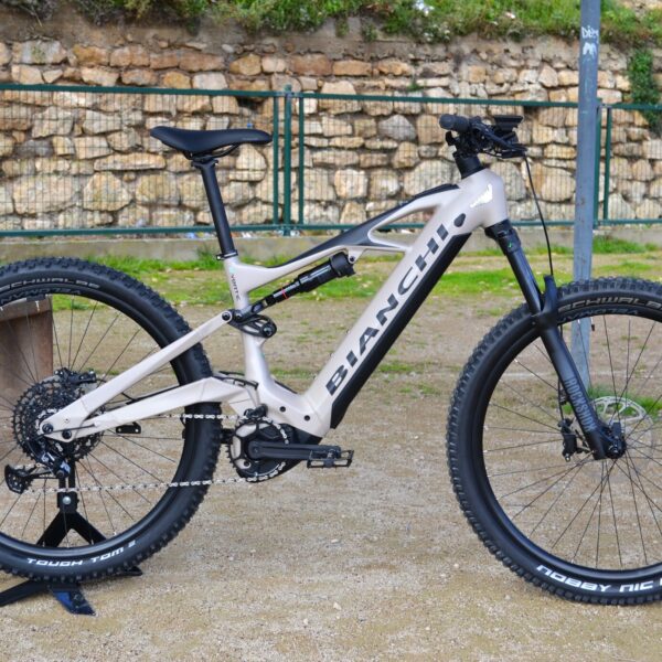 Bicicleta eléctrica de montaña Bianchi E-Vertic FX-Type con doble suspensión, motor central integrado y neumáticos Schwalbe Nobby Nic, estacionada en un entorno rural.