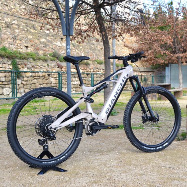 Bicicleta eléctrica de montaña Bianchi E-Vertic FX-Type con doble suspensión, motor central integrado y neumáticos Schwalbe Nobby Nic, estacionada en un entorno rural.