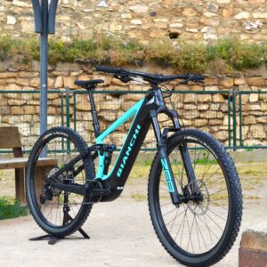 Bicicleta eléctrica de montaña Bianchi T-Tronik FX Pro 29" XT RockShox ZEB con doble suspensión, motor central integrado y neumáticos Schwalbe Nobby Nic, estacionada en un entorno rural.