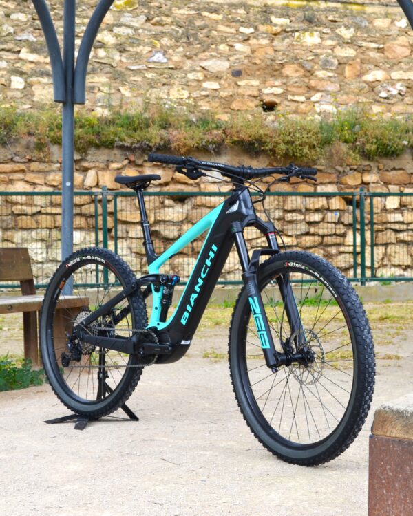 Bicicleta eléctrica de montaña Bianchi T-Tronik FX Pro 29" XT RockShox ZEB con doble suspensión, motor central integrado y neumáticos Schwalbe Nobby Nic, estacionada en un entorno rural.
