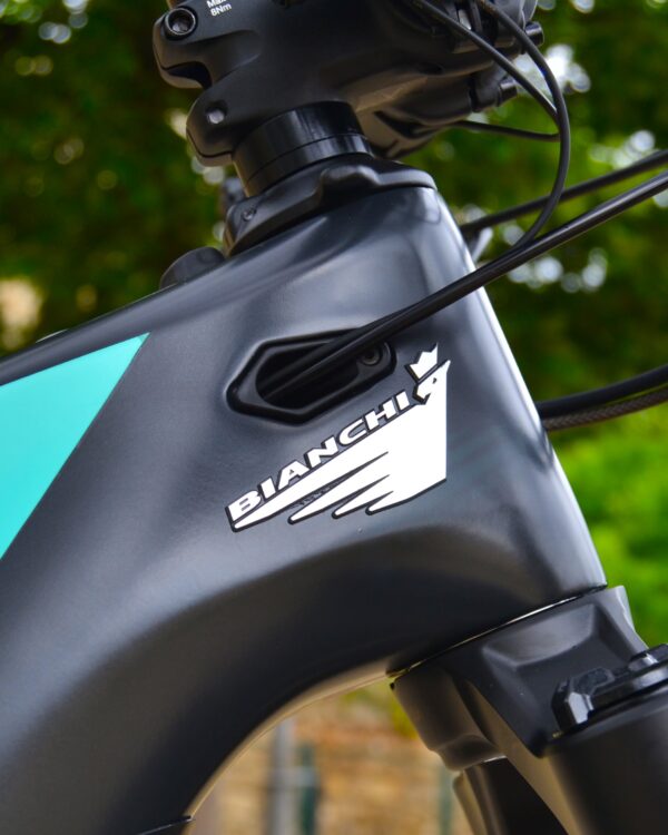Bicicleta eléctrica de montaña Bianchi T-Tronik FX Pro 29" XT RockShox ZEB con doble suspensión, motor central integrado y neumáticos Schwalbe Nobby Nic, estacionada en un entorno rural.