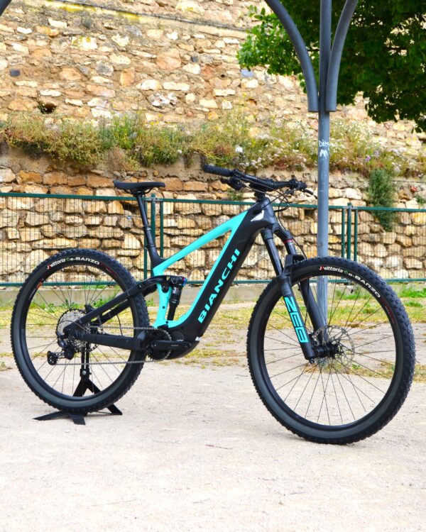 Bicicleta eléctrica de montaña Bianchi T-Tronik FX Pro 29" XT RockShox ZEB con doble suspensión, motor central integrado y neumáticos Schwalbe Nobby Nic, estacionada en un entorno rural.