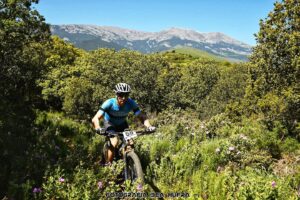 Ciclistas del equipo Bikes Moncayo atravesando un sendero boscoso durante la carrera, rodeados de vegetación y con vistas al Moncayo.